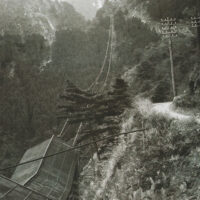 新道中継所と東平街道：標高約500m。東平方向を望んだ風景。索道に搬器が連なっている。向かって右側が下りで鉱石を運搬。左が生活物資を運搬。遠登志と東平を結ぶ東平街道沿いに電柱が見える。
