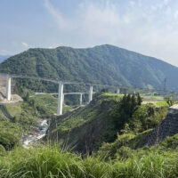 北向山北面全景(北向谷原始林)：かつてこの8合目付近を東西に横断する南郷往還が走っていた。遠くから微かにそれを辿る杉並木が見える。手前は新阿蘇大橋と長陽大橋。(数鹿流ヶ滝付近から)
