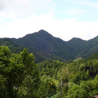 越上山の遠望：ここから見上げる越上山は三角形の山容で南峯と北峰に分かれ、右隣は雨乞い塚と呼ばれています。北峰はチャート岩質で祠に修験者の碑伝が残されています。
